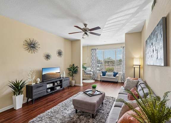 A living room with a grey sofa, a grey coffee table, a black cabinet, a ceiling fan, and a painting on the wall.