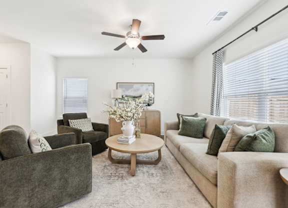 A living room with a grey couch, a brown armchair, a coffee table, and a ceiling fan.