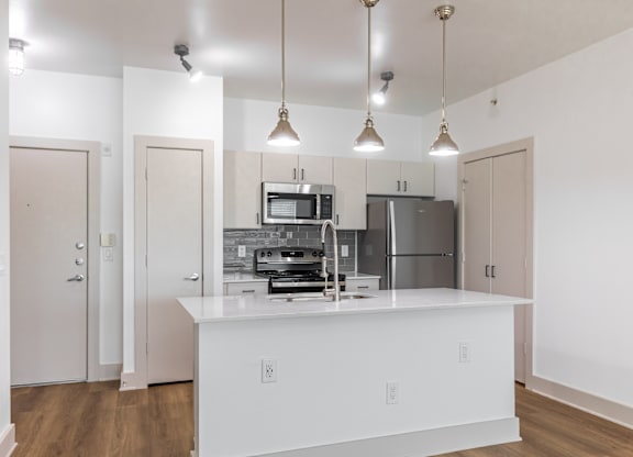 A kitchen with a white island and pendant lights.