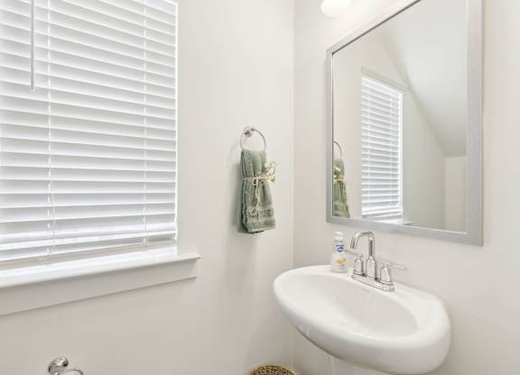 A white sink in a bathroom with a mirror and a window with blinds.