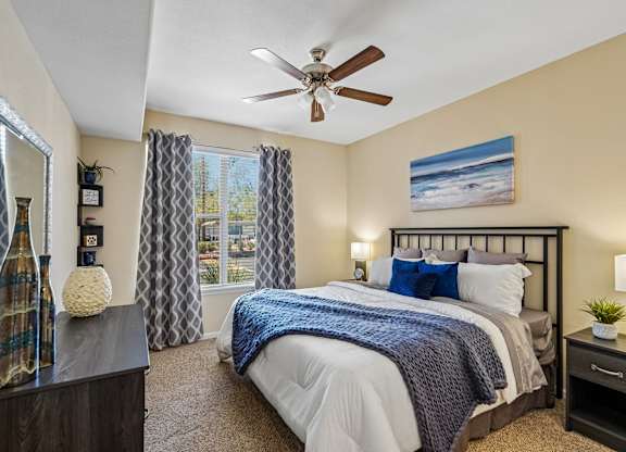 A bedroom with a large bed, a ceiling fan, and a painting on the wall.