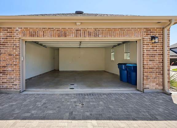 A garage with a brick wall and a blue trash bin.