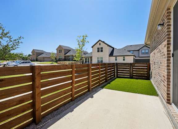 A wooden fence separates a house from a green lawn.