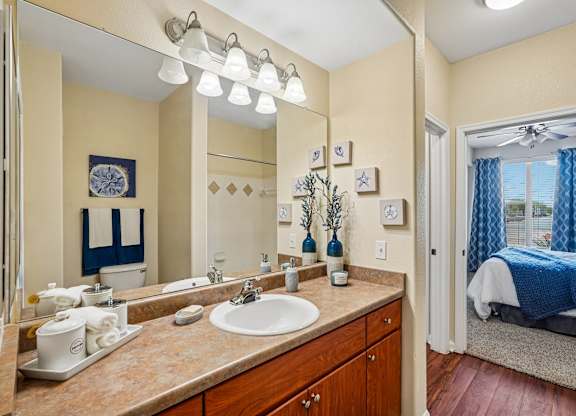 A bathroom with a sink, mirror, and a bed in the background.