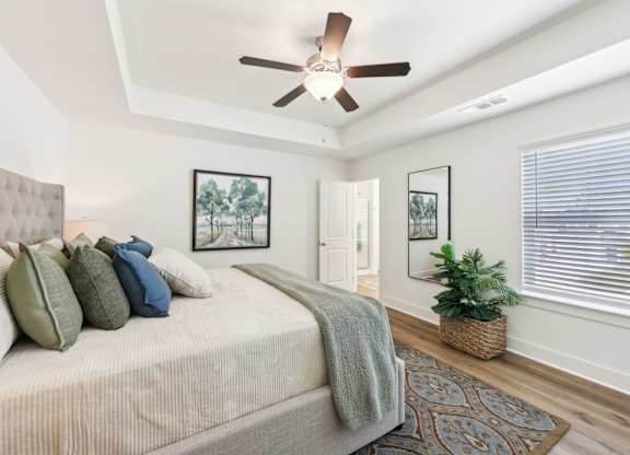 A bedroom with a bed, pillows, a ceiling fan, and a rug.