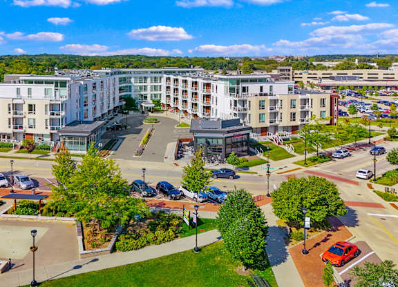 A view of a city with apartment buildings, trees, and a parking lot.