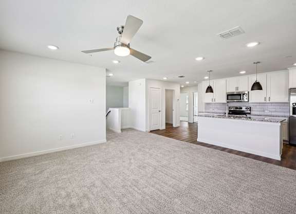 A spacious living room with a ceiling fan and a kitchen area in the background.