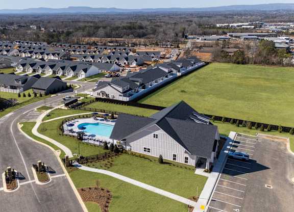 A bird's eye view of a residential area with houses, a swimming pool, and a parking lot.