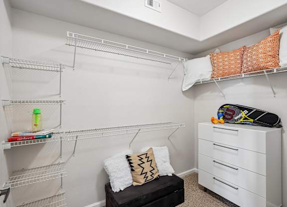A white closet with a bench and a white dresser.