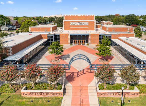 The Lewisville Grand Theater is a large, modern building with a red brick exterior and a spacious entrance.