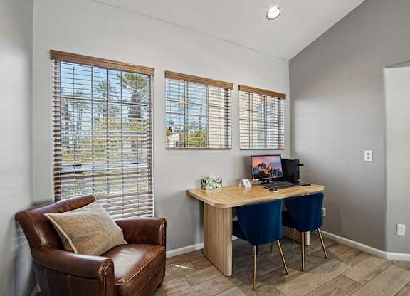 A room with a brown leather chair, a wooden desk with two chairs and a window with blinds.