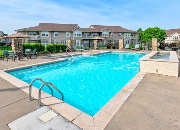 A large swimming pool with a diving board in the foreground and apartment buildings in the background.