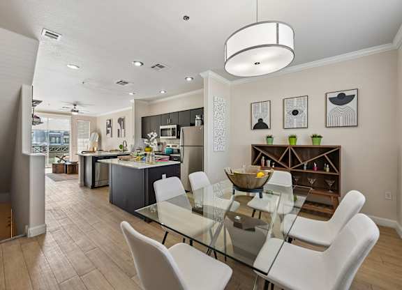 A modern kitchen with a glass dining table and white chairs.