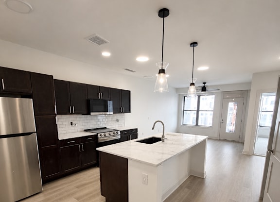 Dog-Friendly Apartments in Kokomo, IN - The Elwood Apartments - Kitchen With Dark Cabinets, Stainless Steel Appliances, A White Island, Pendant Lights, And Luxury Vinyl Plank Flooring.