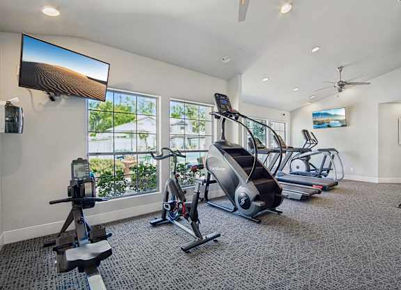 A spacious gym with a variety of equipment including treadmills, elliptical machines, and a television.