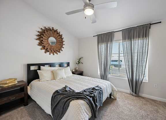 A bedroom with a bed, a ceiling fan, and a mirror on the wall.