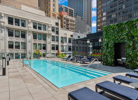 A pool surrounded by chairs and a green wall.