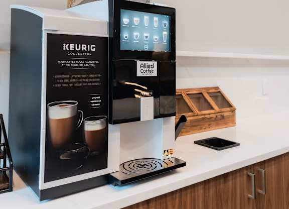 A Keurig coffee machine sits on a counter with a box and a display screen.