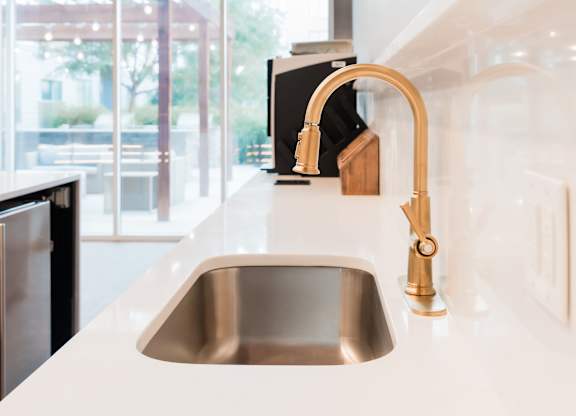 A kitchen sink with a gold faucet and a black dishwasher.