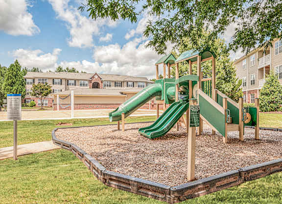 A playground with a green slide and a wooden structure.