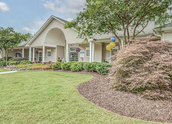 A house with a well-maintained lawn and a tree with a bush in front of it.