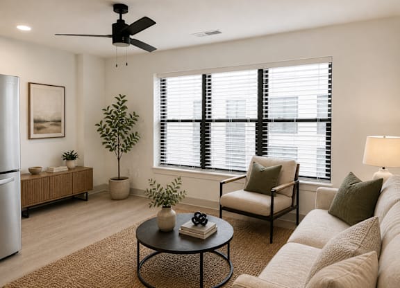 Kokomo, IN, Pet-Friendly Apartments - The Elwood Apartments - Living Room Featuring A Neutral Sofa, Armchair, Round Coffee Table, Indoor Plants, And Large Windows.