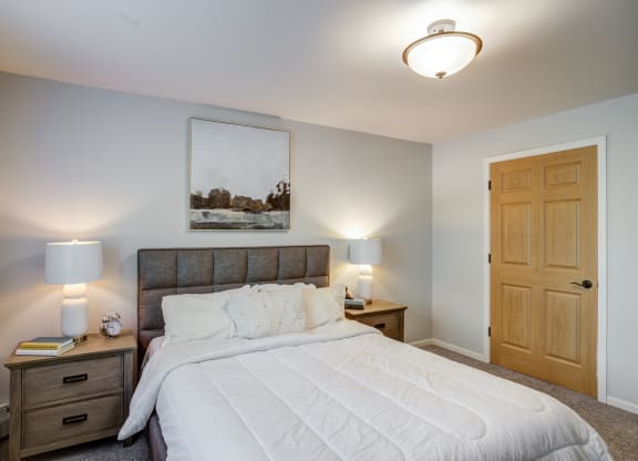 a bedroom with a large white bed and a wooden closet at Birchwood Apartment Homes in Maple Grove, MN