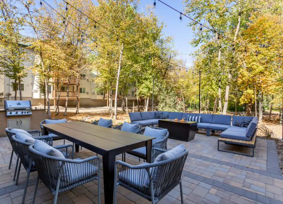 a patio with couches tables and chairs and trees at Birchwood Apartment Homes in Maple Grove, MN