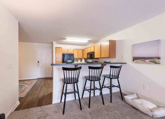 A kitchen area with a bar and chairs.