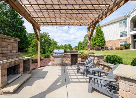 A patio with a fireplace and chairs under a wooden pergola.