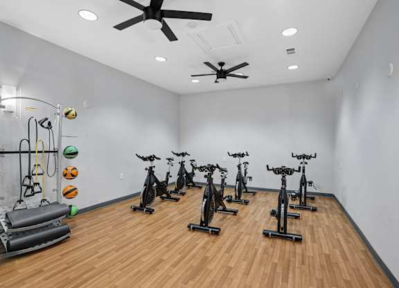 A room with a white wall and a wooden floor with a row of exercise bikes.