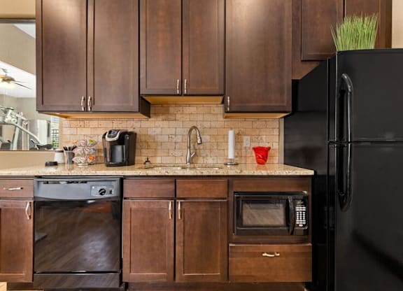 A black refrigerator is on the right side of a kitchen with brown cabinets.