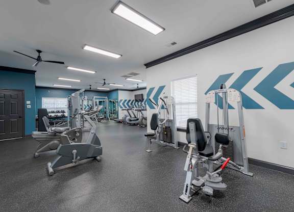 A gym with a variety of equipment including treadmills, weights, and a fan.