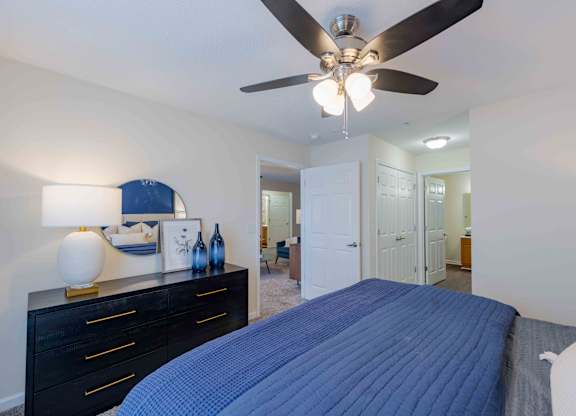 A bedroom with a blue bedspread and a ceiling fan.