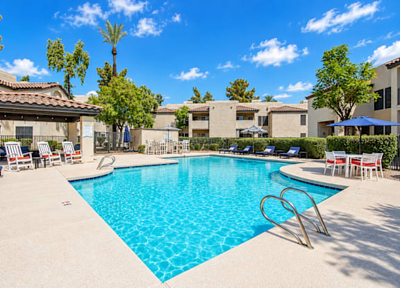 A swimming pool surrounded by chairs and trees.