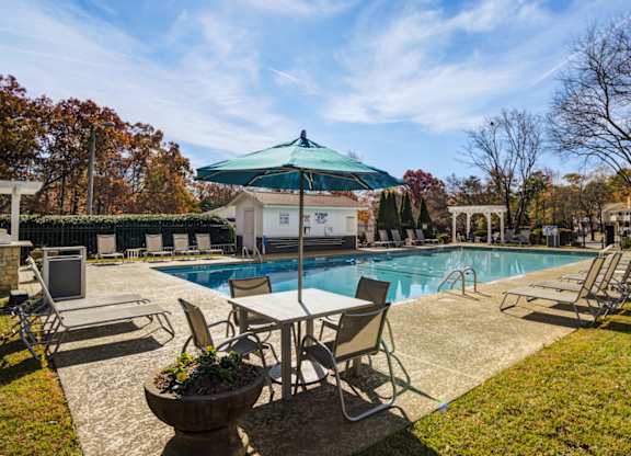 A pool area with chairs and a table under a green umbrella.