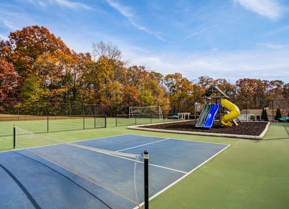A tennis court with a blue surface and a yellow slide in the background.