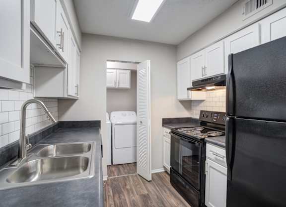 A black refrigerator is in the kitchen with white cabinets.