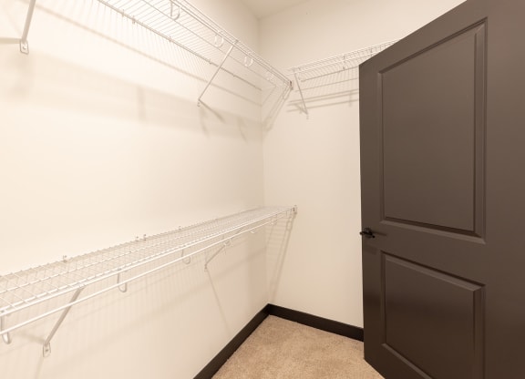 a walk in closet with white metal shelves and a black door