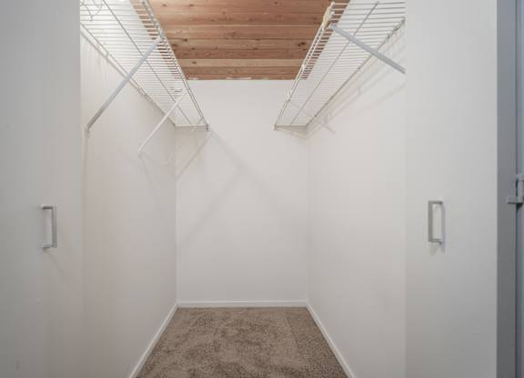 A white room with a carpeted floor and a wooden ceiling with metal beams.