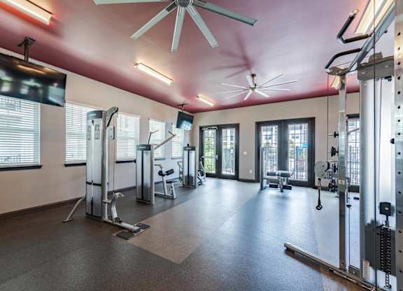 A gym with a variety of equipment including treadmills, weights, and a fan.