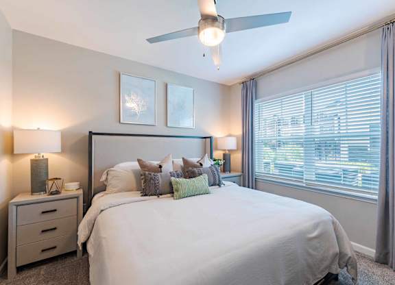 A bedroom with a large bed, a ceiling fan, and two lamps.