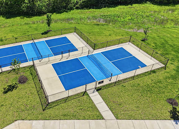 A tennis court surrounded by a fence and green grass.