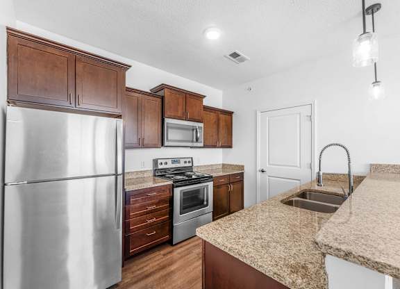 A kitchen with a stainless steel refrigerator, microwave, oven, and sink.
