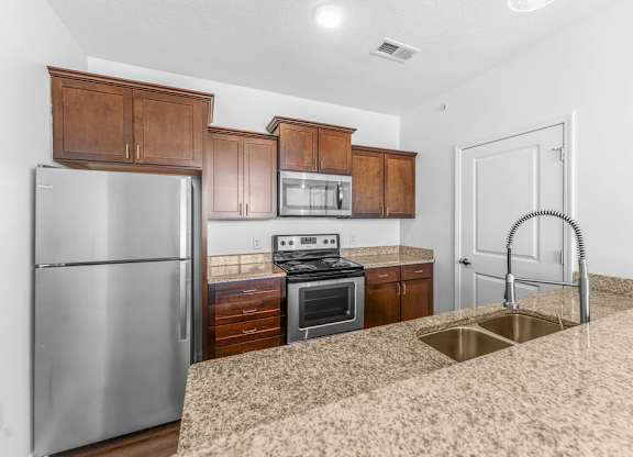 A kitchen with a stainless steel refrigerator, microwave, oven, and sink.