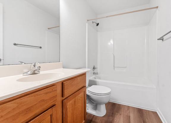 A white toilet sits in a bathroom with a wooden vanity and a walk-in shower.