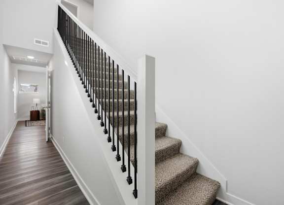 A staircase with a beige carpeted runner and black balusters.
