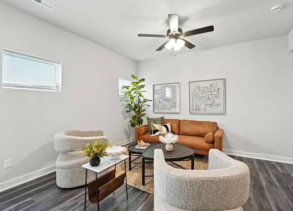 A living room with a brown couch, a white chair, and a plant.