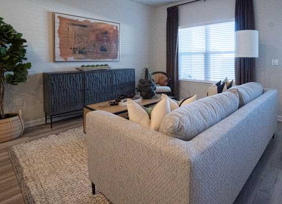 A living room with a grey couch and a painting on the wall.