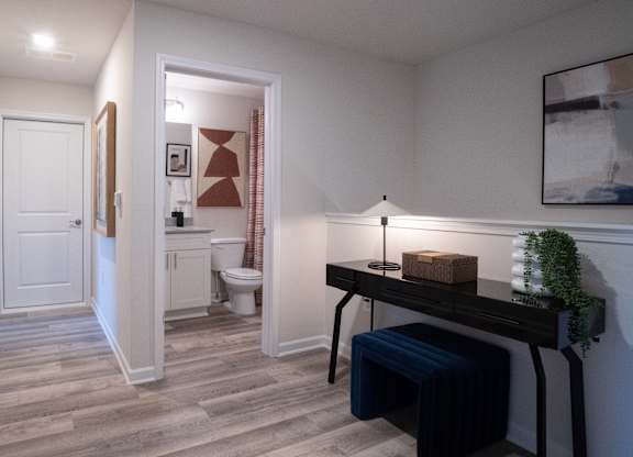 A hallway with a bench and a lamp on a desk.